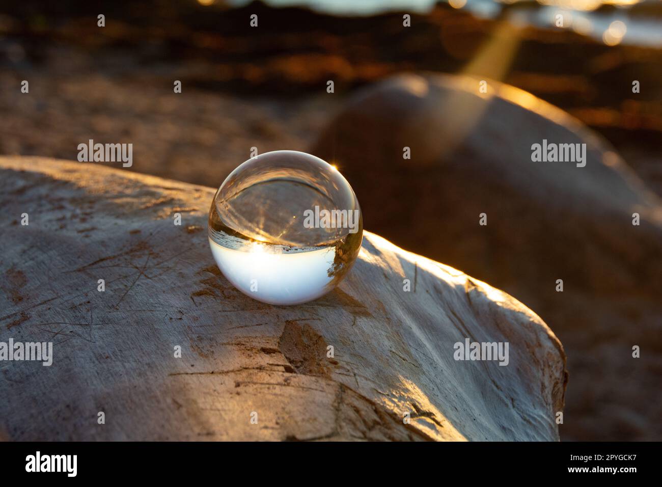 Ball made of glass lies on a stone in which the beach and the sea are ...