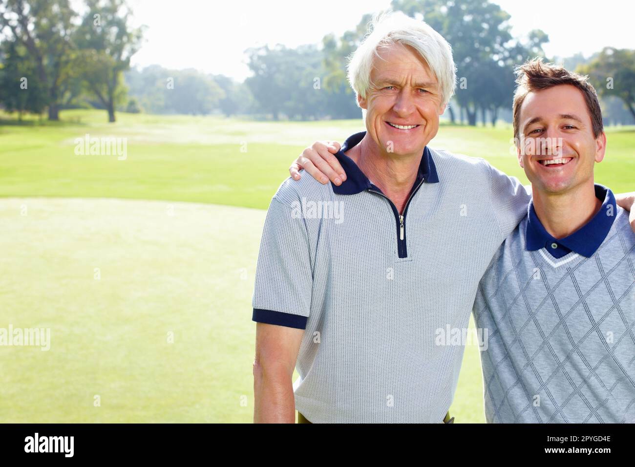 Father and son smiling. Portrait of father and son on the golf course standing with arms around and smiling. Stock Photo