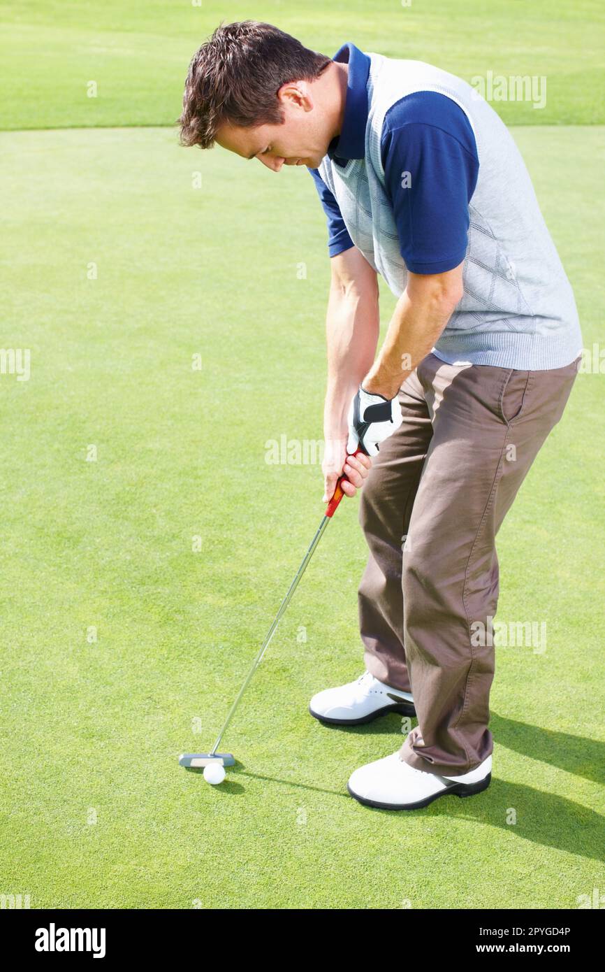 Male golfer ready to putt the ball. Male golfer standing on the putting green and taking his position to putt the ball. Stock Photo
