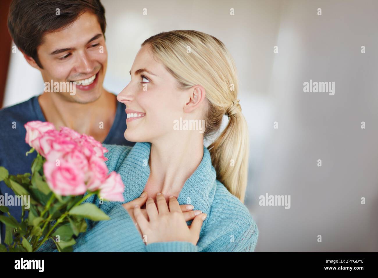 Their love is in bloom. an affectionate young man giving his beautiful young wife a bouquet of pink roses. Stock Photo