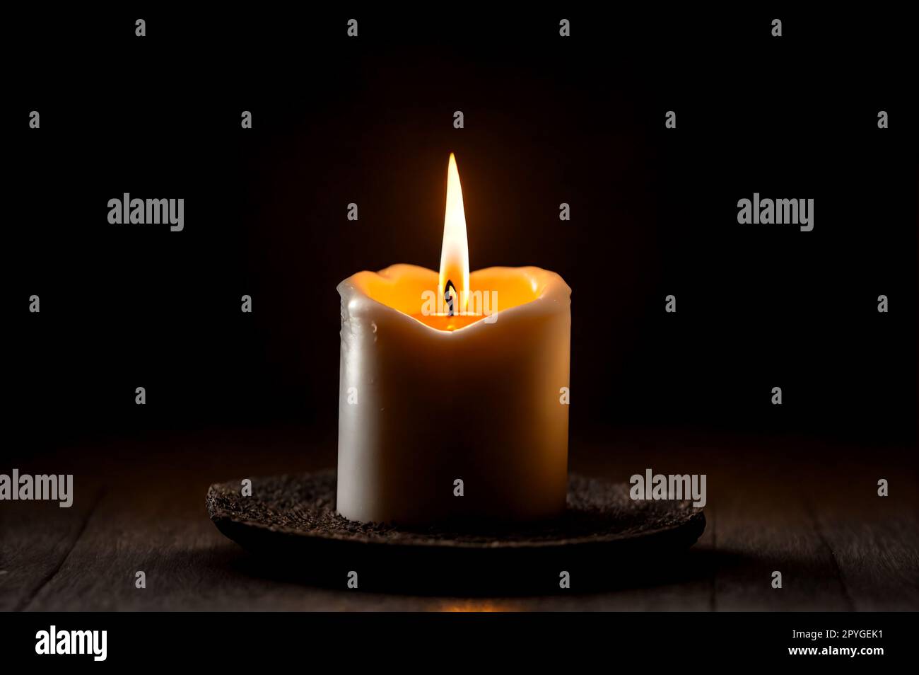 Small burning candle on wooden floor with dark background Stock Photo