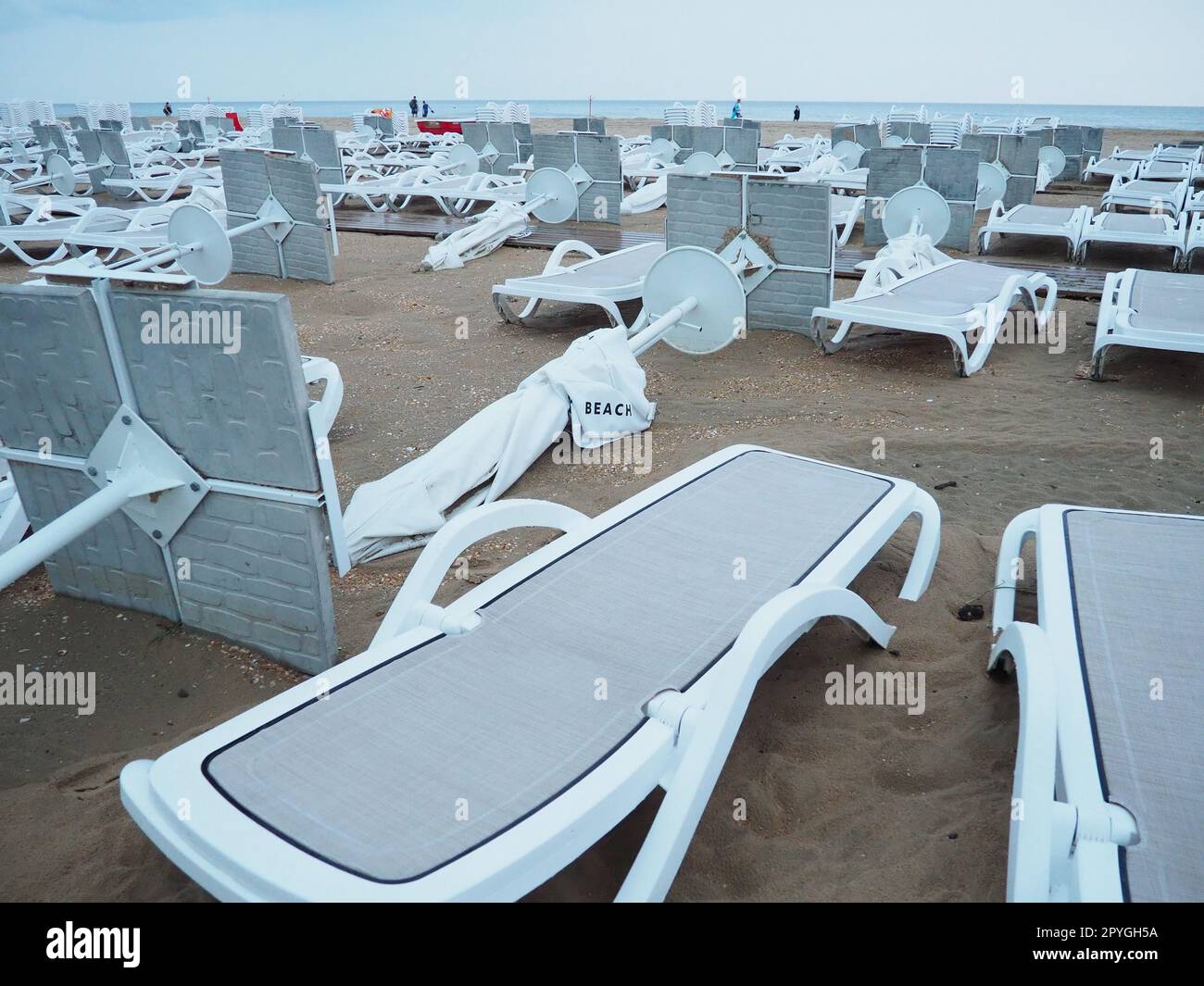 A beach umbrella lay folded on a sandy beach after bad weather. Storm at sea. End of the beach season due to typhoon and cyclone. Loungers, umbrellas and hotel furniture. Wind-upturned structures Stock Photo