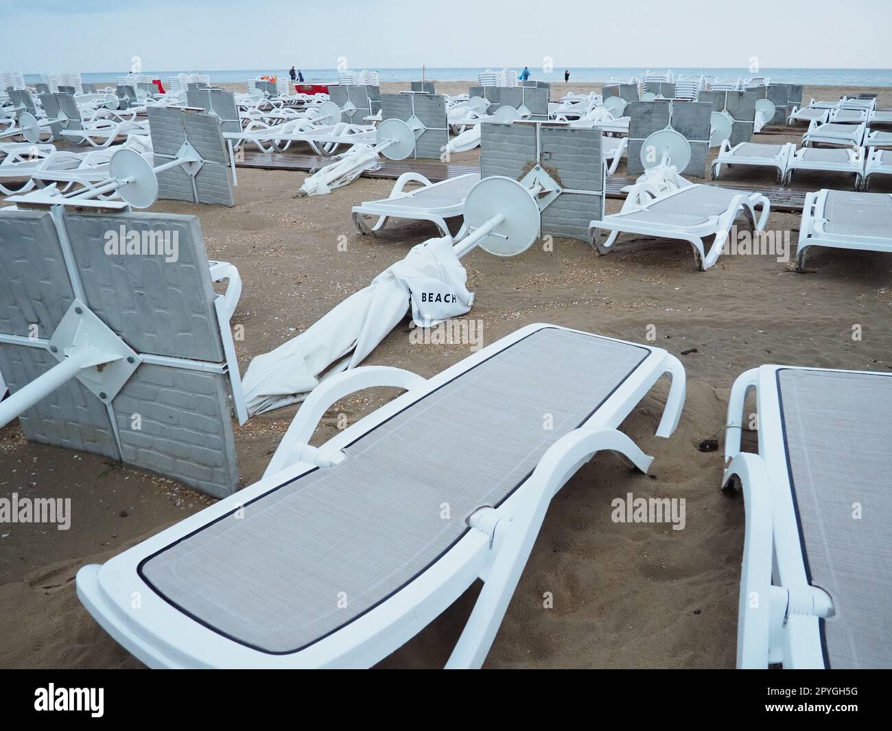 A beach umbrella lay folded on a sandy beach after bad weather. Storm at sea. End of the beach season due to typhoon and cyclone. Loungers, umbrellas and hotel furniture. Wind-upturned structures Stock Photo