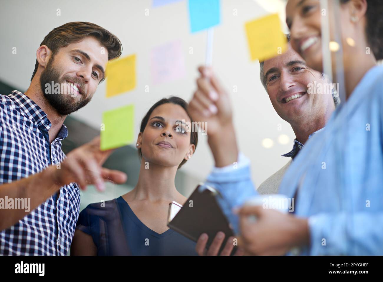 Teamwork makes the dream work. coworkers arranging sticky notes on a glass wall during a brainstorming session. Stock Photo