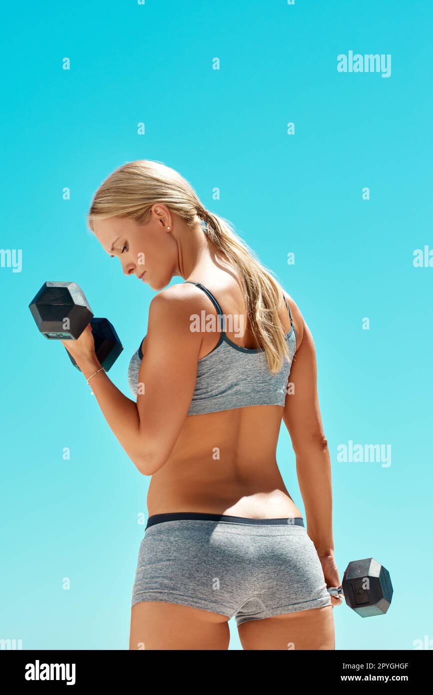 Fitness is the key to life. Rearview shot of an attractive young woman exercising with dumbbells outside. Stock Photo
