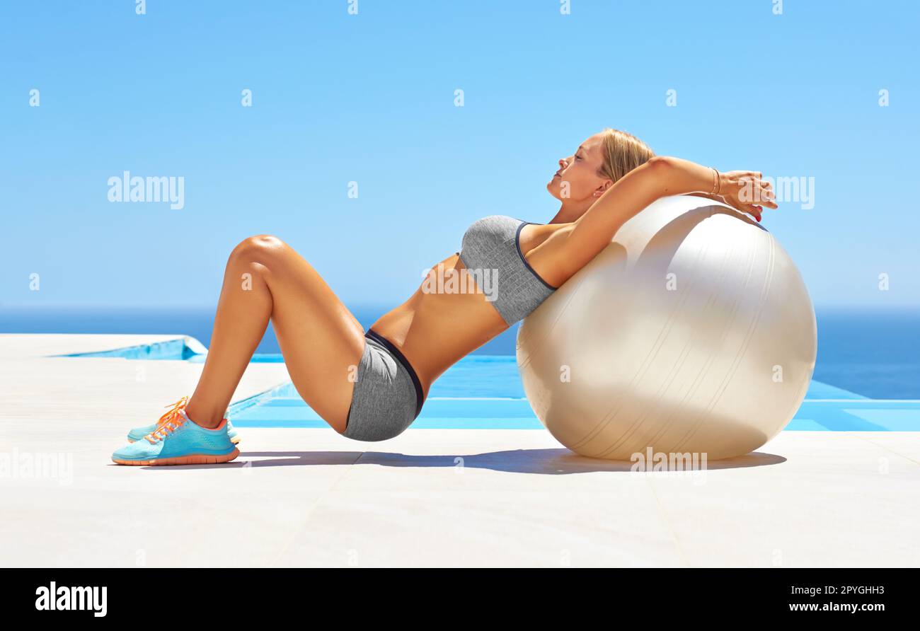 Working out from head to toe. an attractive young woman working out with an exercise ball by a swimming pool. Stock Photo