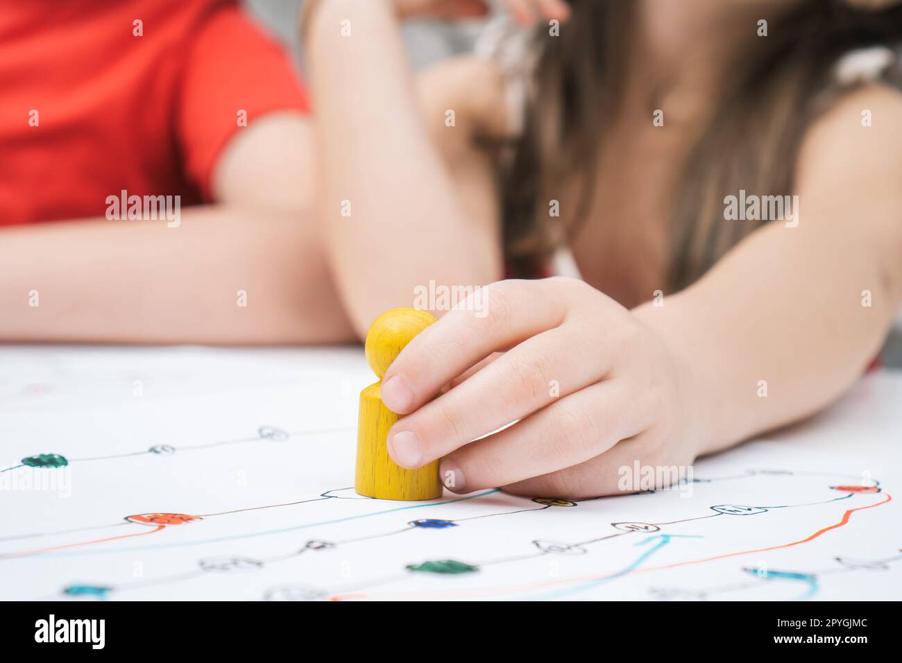 Close up child hand with yellow game paw figure on creative art map. Girl and other kids playing board game with pieces Stock Photo