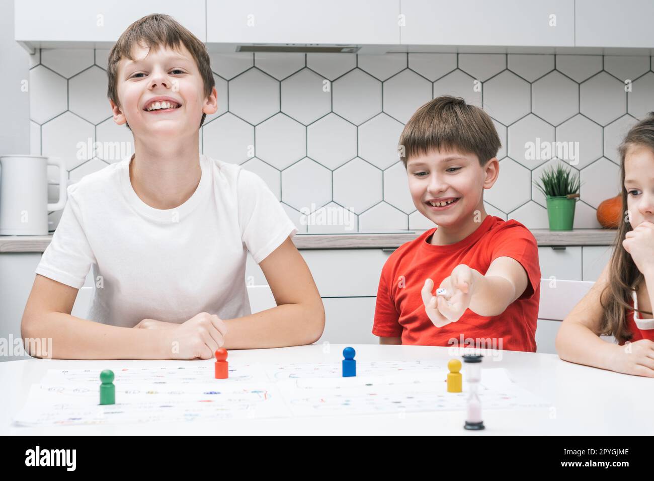 Smiling blissful children playing board game with pieces and dice with time limit. Family fun game. Educational strategy Stock Photo