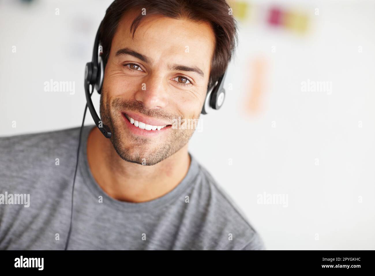 On the line to help. Closeup portrait of a handsome young man wearing a headset and smiling at the camera. Stock Photo