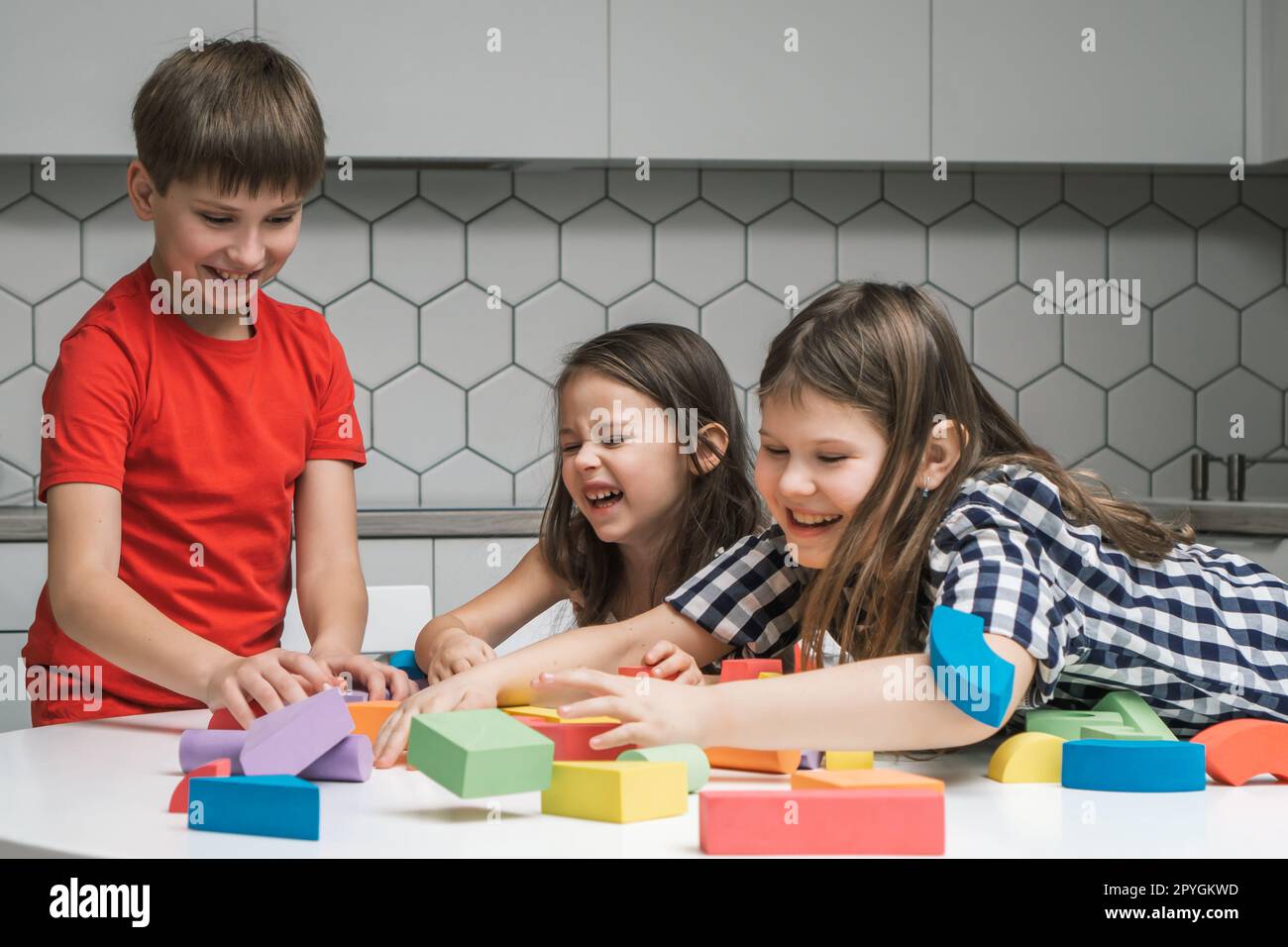 Laughing, funny and playful children of girls fooling around and boy playing with colorful bricks and building elements Stock Photo