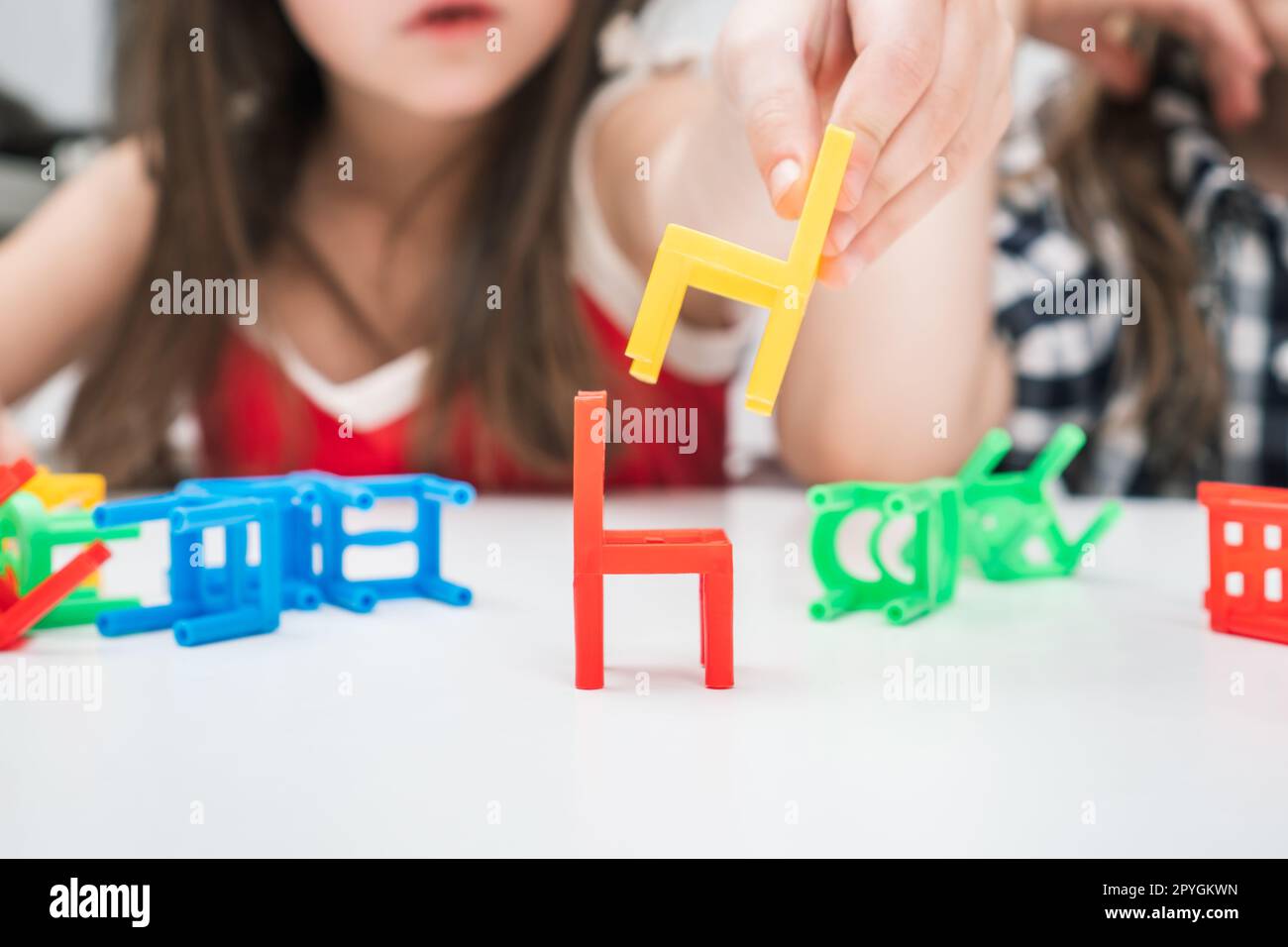Cropped blurred little girl build pyramid tower from colorful chair toys, play chair ladder tower board game on table Stock Photo