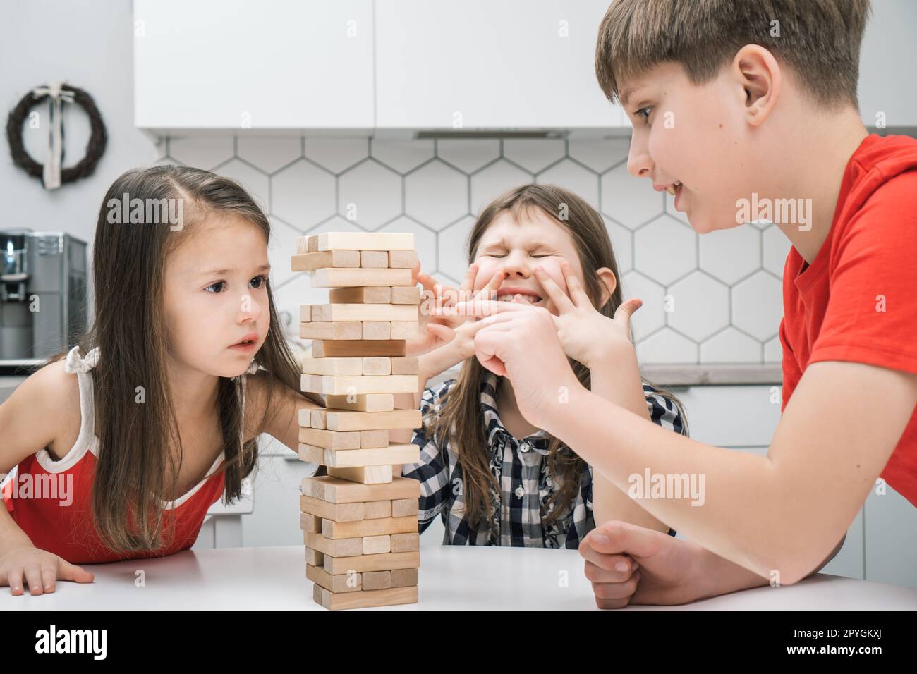 Nervous worried passionate kids playing board balance wooden brick tower game. Boy trying to move wooden cube out line Stock Photo