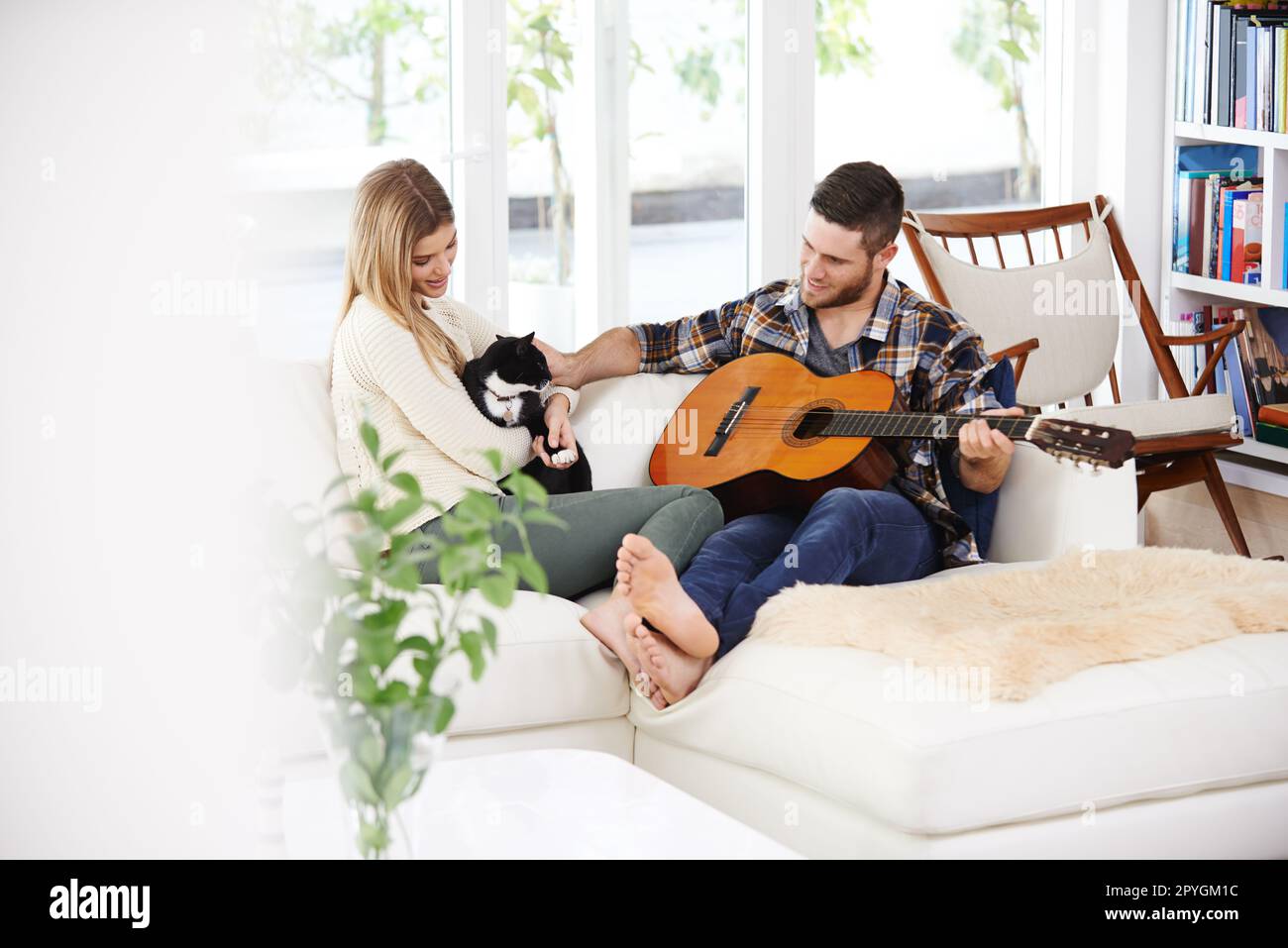 Playing to his number one fans. a young man playing the guitar for his girlfriend while sitting on their sofa. Stock Photo