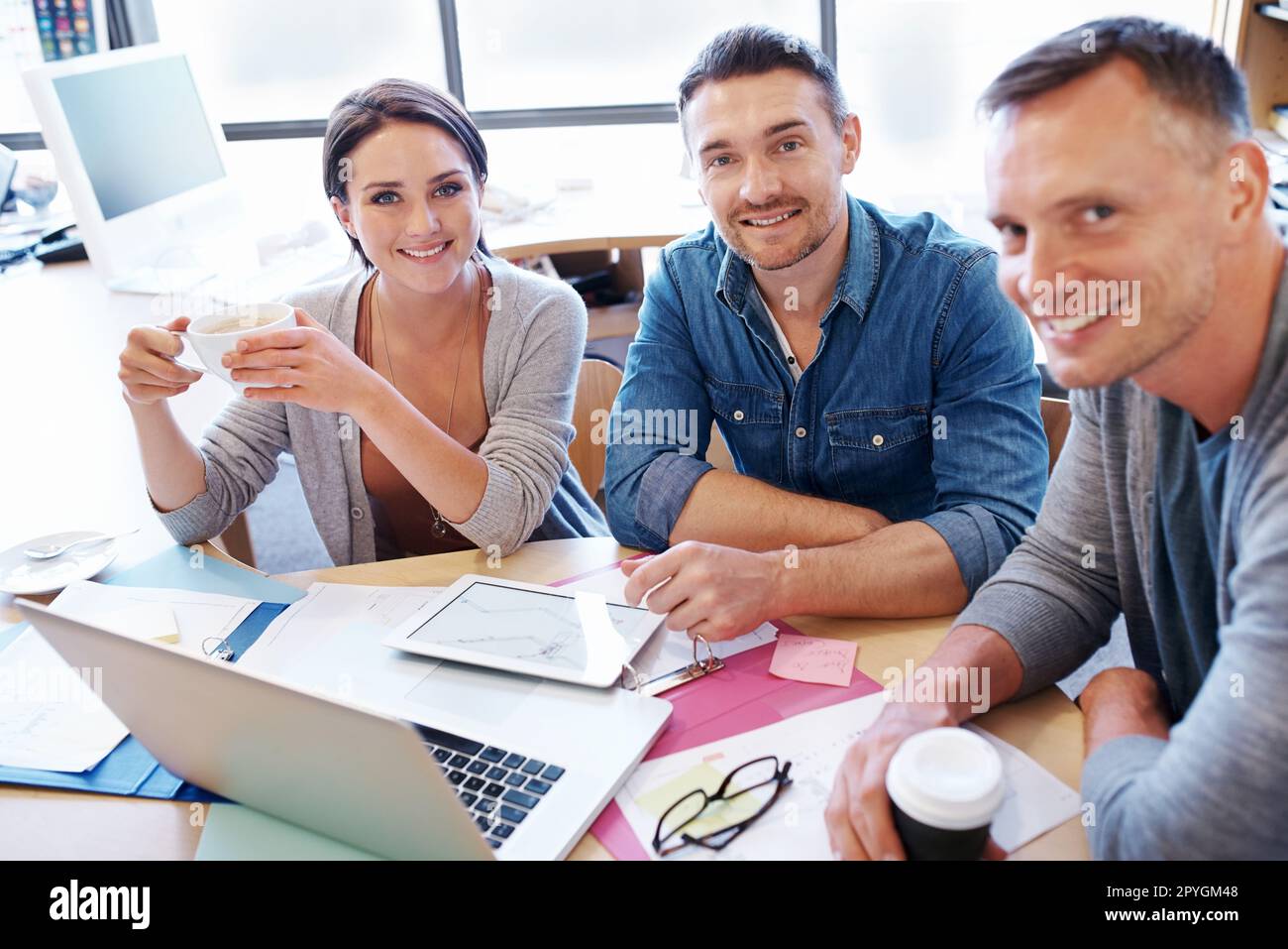 We keep meetings informal here. three coworkers having a discussion at a table. Stock Photo