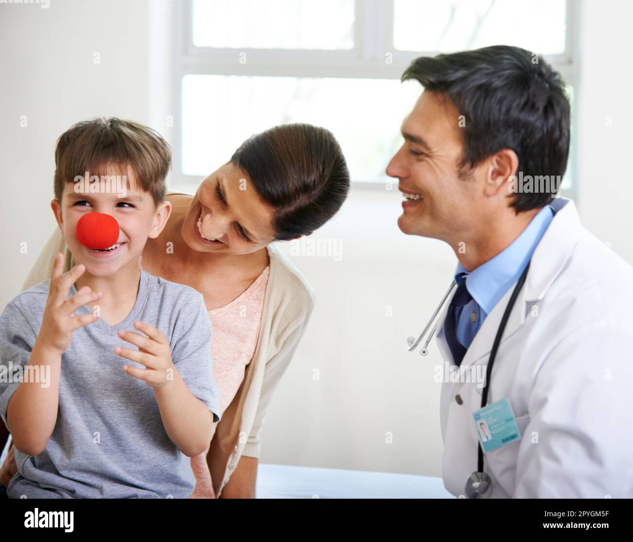 The first sign of flu is a red nose. a cute young boy playing with a clowns nose in the doctors room. Stock Photo