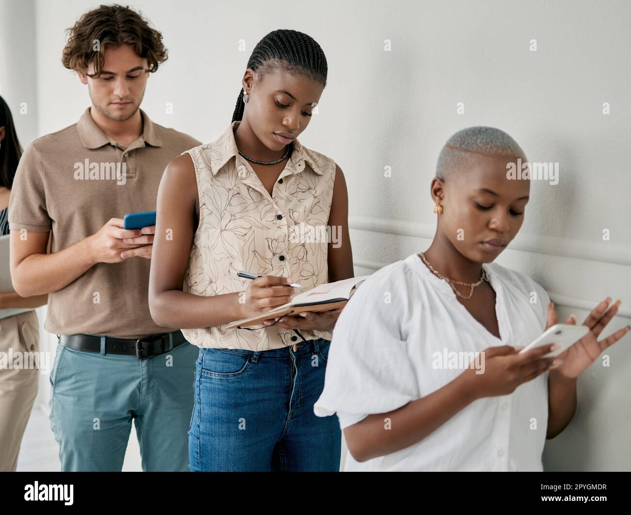 Recruitment, office and business people waiting for an interview or hr meeting while writing notes and networking. Diversity, hiring and professional job candidates standing in line in the workplace. Stock Photo