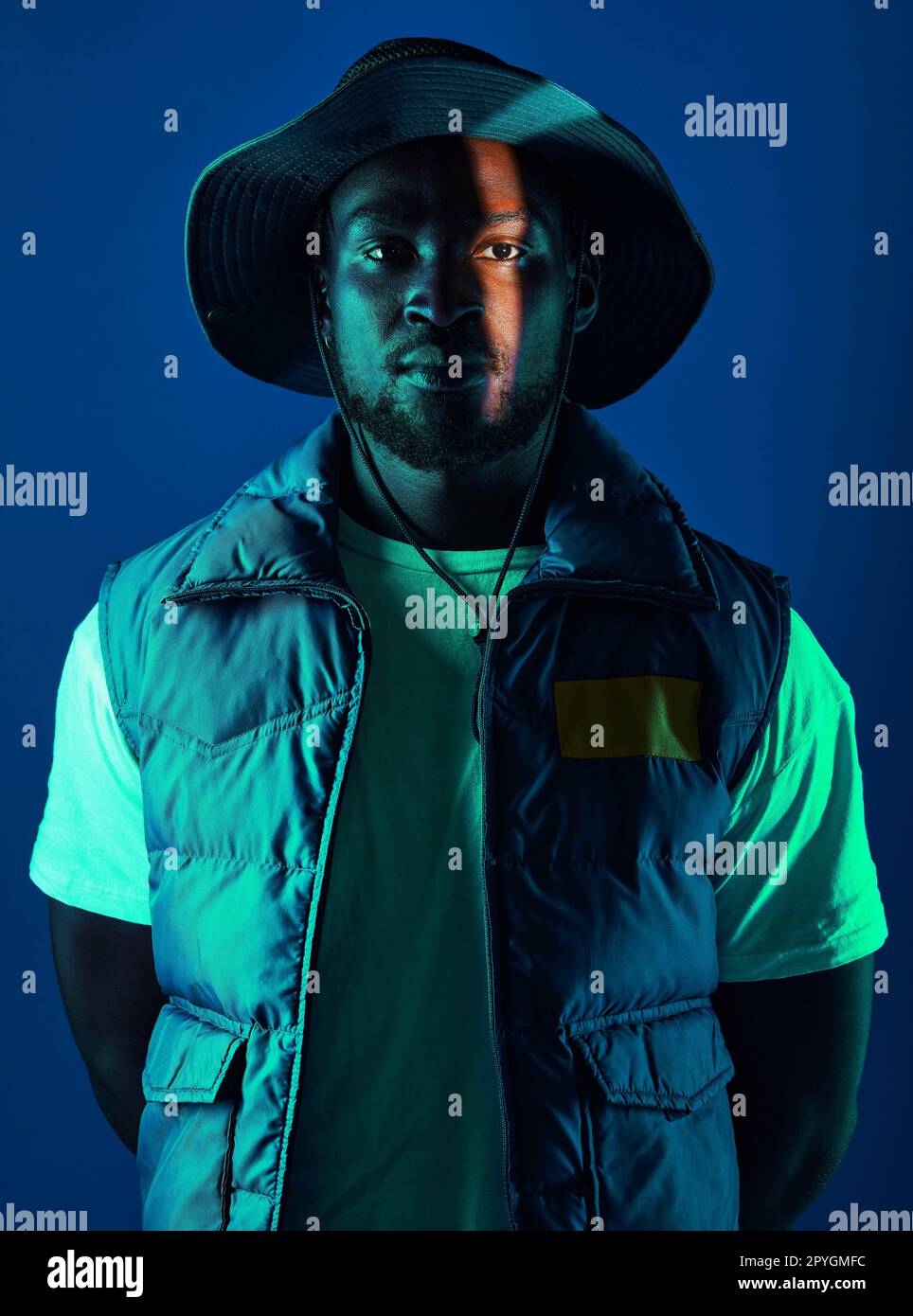Trendy, casual and portrait of a black man in a studio with a cool, stylish and edgy outfit. Fashion, style and African male model with modern clothes posing while isolated by a blue background. Stock Photo