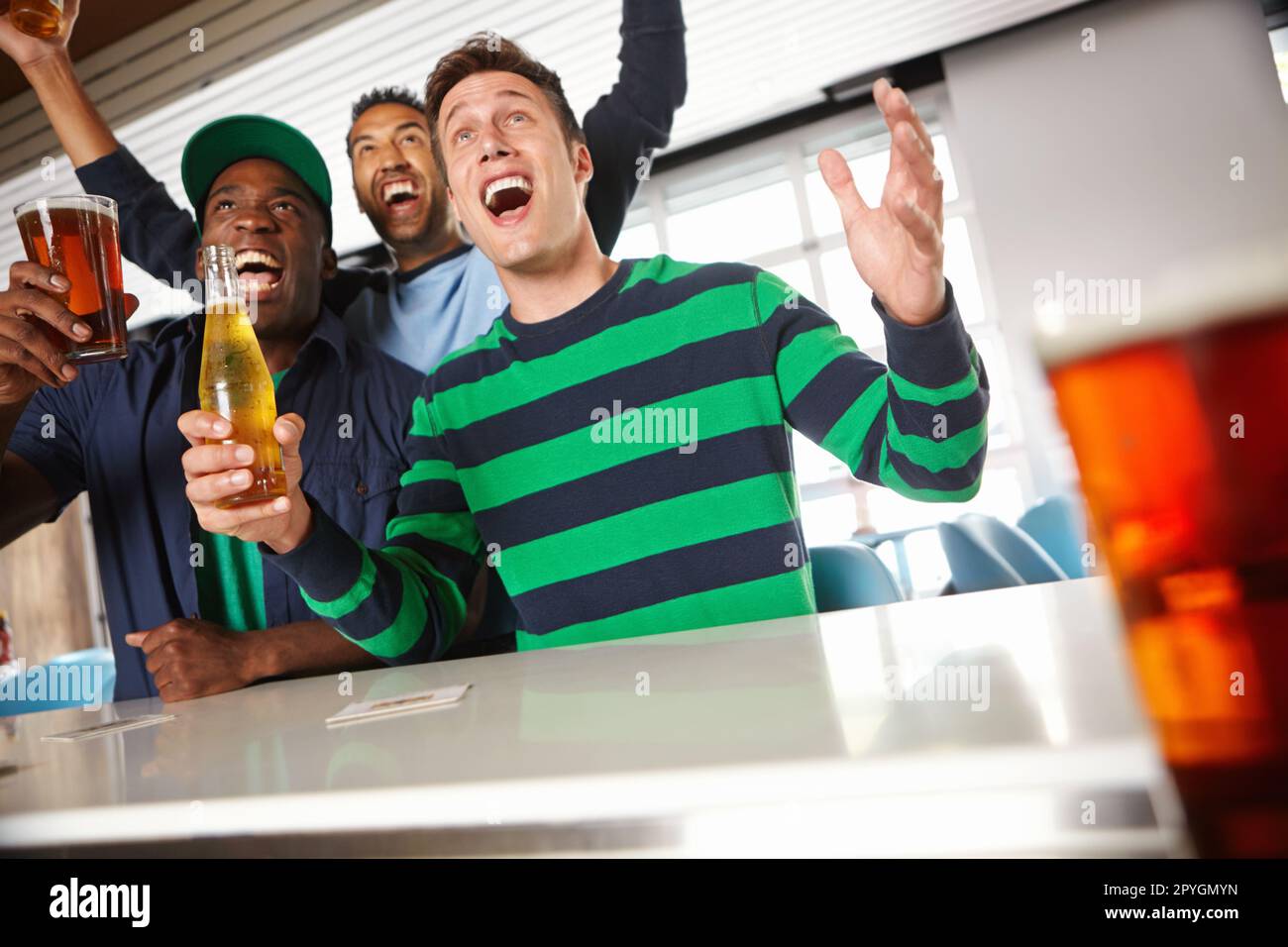 Catching the game at their local bar. Low view of a group of friends cheering on their favourite sports team at the bar. Stock Photo