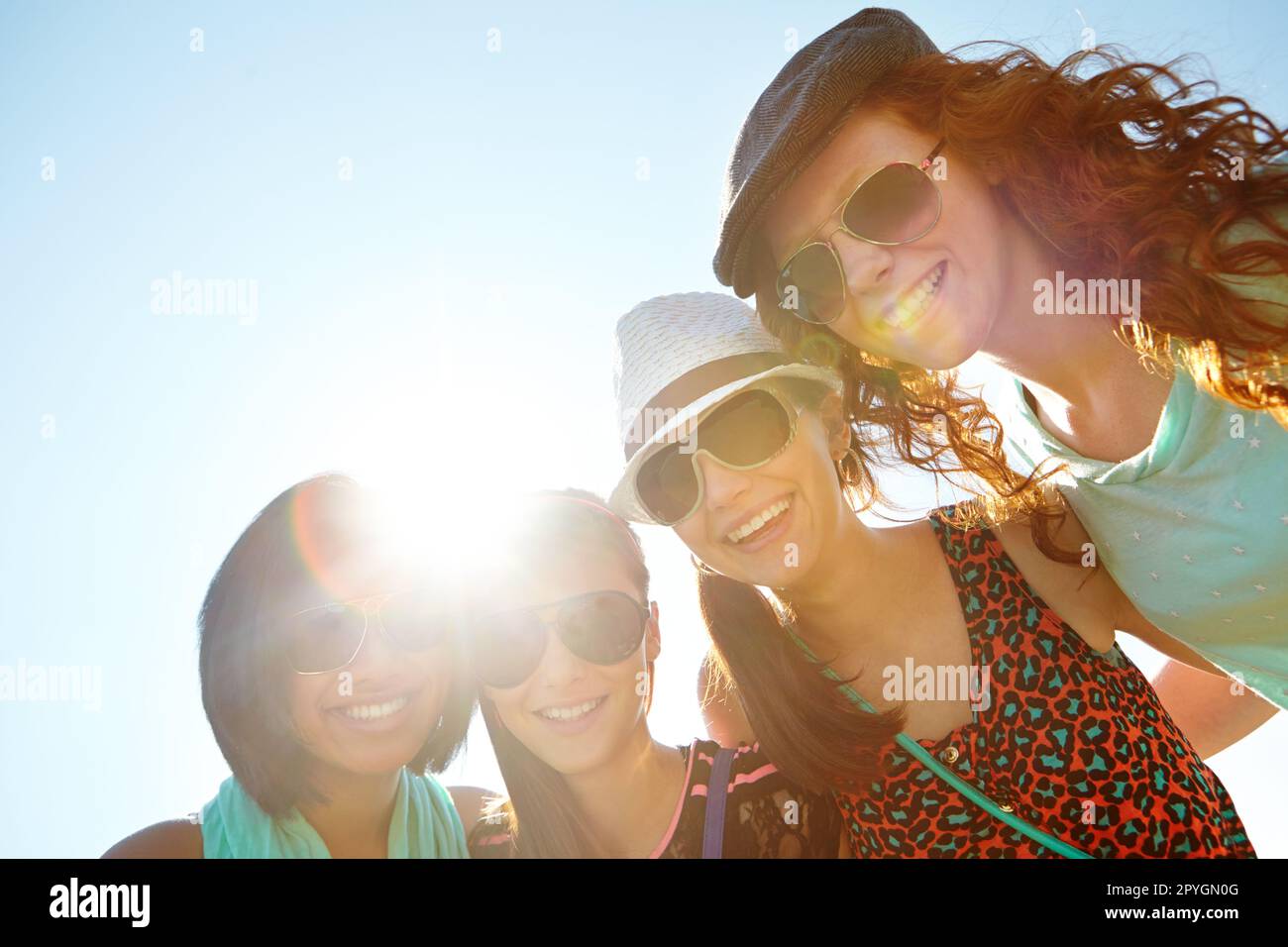 Summertime sisterhood. A group of four teenage girls smiling with their arms around each others shoulders. Stock Photo
