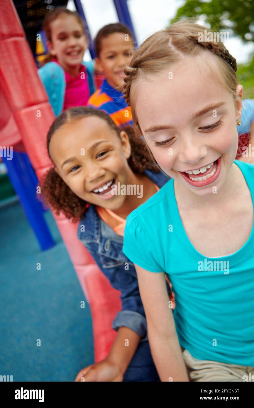 Best pals. A happy group of multi-ethnic children sitting happily on a slide in a play park. Stock Photo
