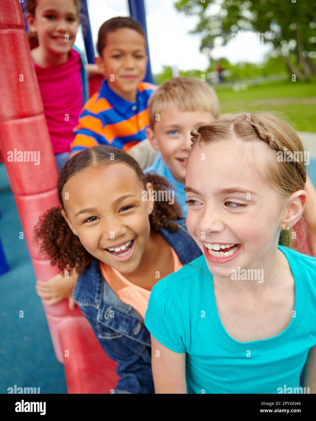 Enjoying time spent together. A happy group of multi-ethnic children sitting happily on a slide in a play park. Stock Photo
