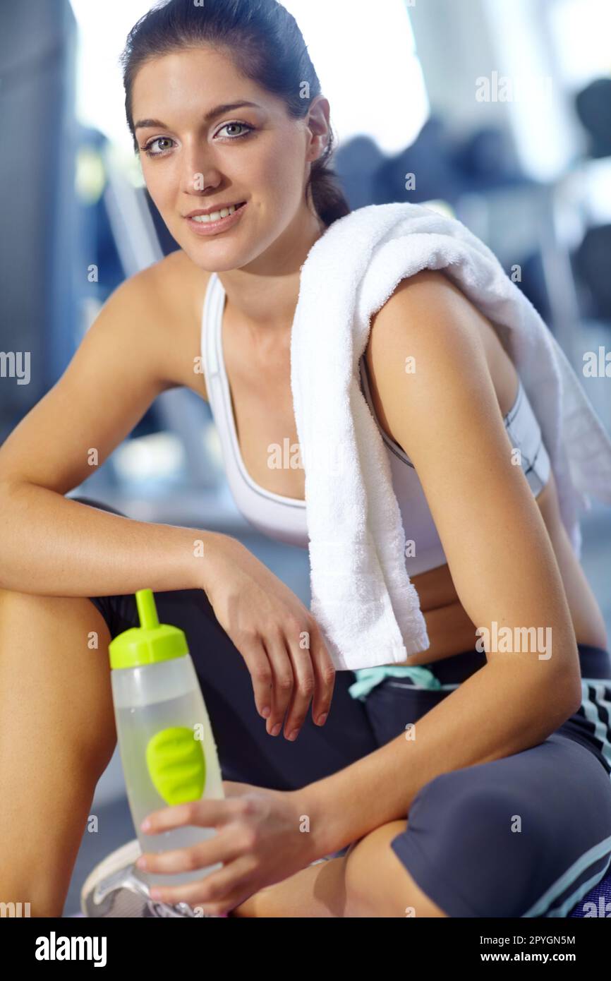 Time to catch my breath. A beautiful young woman sitting at the gym taking a break and having a drink of water. Stock Photo