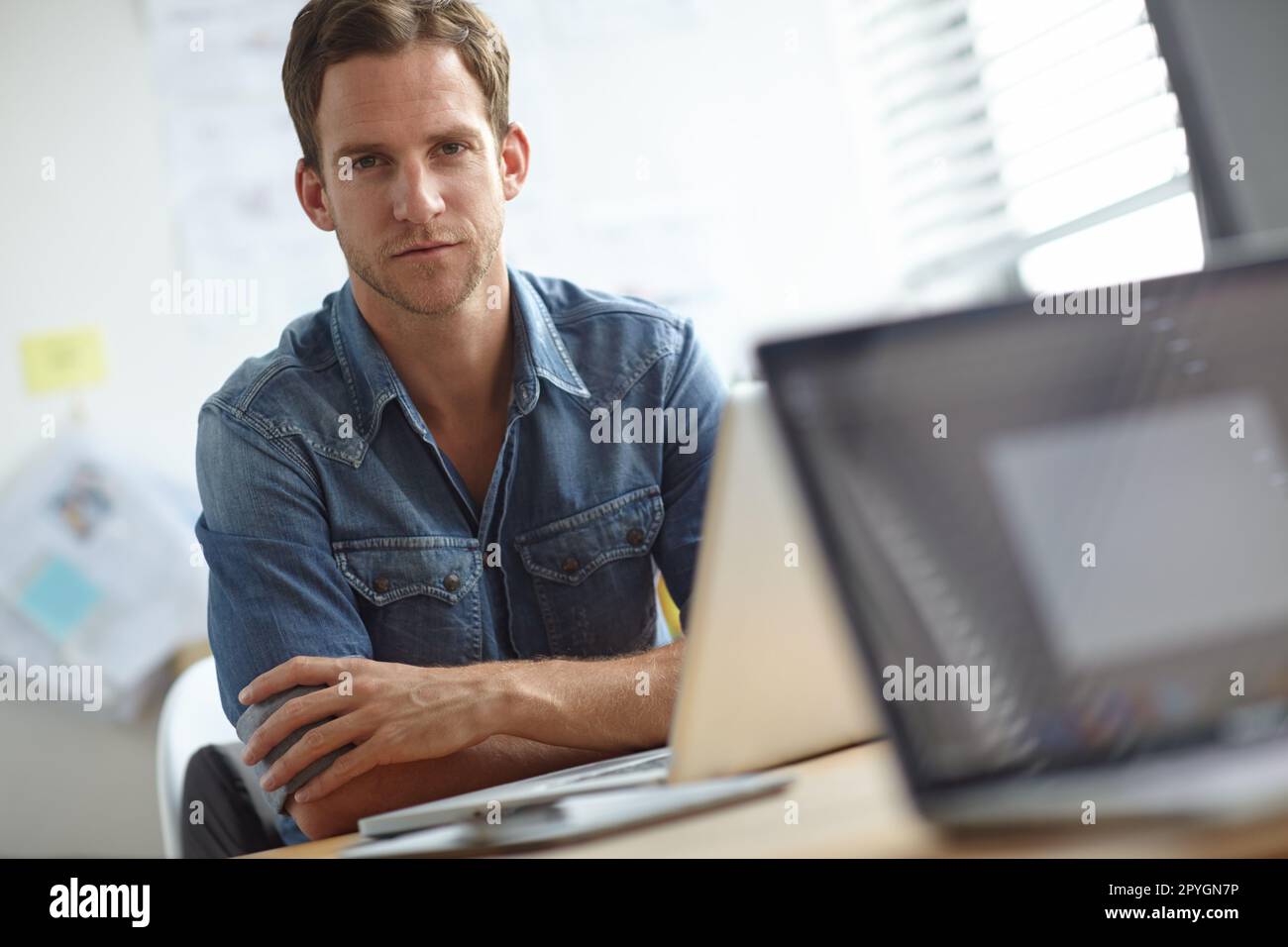 Serious about work. A young man sitting at his desk while looking at the camera. Stock Photo