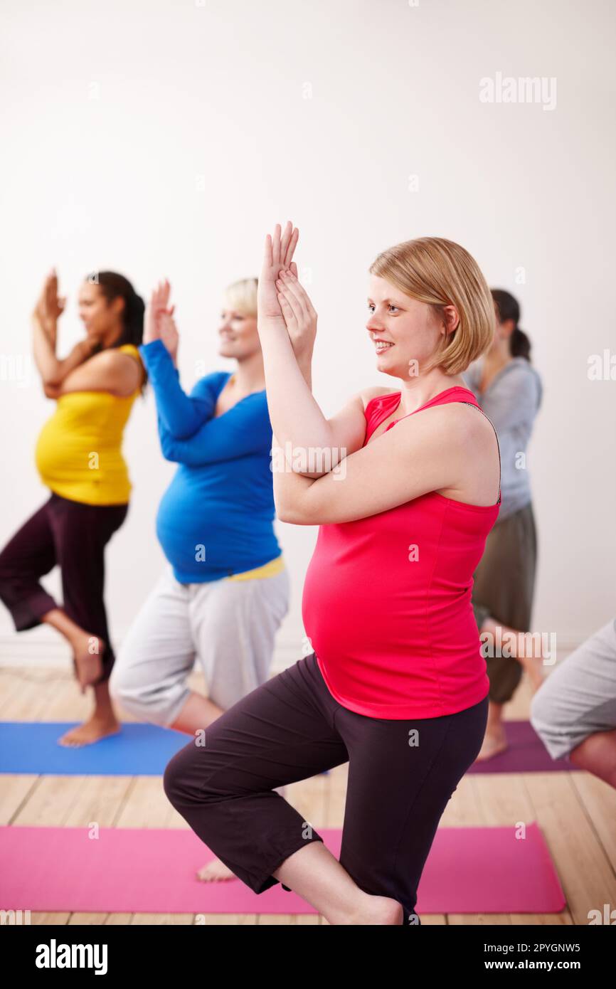 Keeping the balance. A multi-ethnic group of pregnant women balancing on one leg with their arms entwined in a yoga pose. Stock Photo
