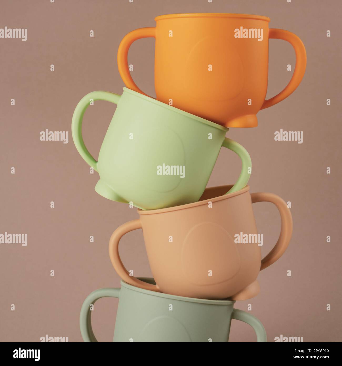 Modern colorful pastel silicone cups stacked in column on brown background. Baby tableware, first feeding. Stock Photo