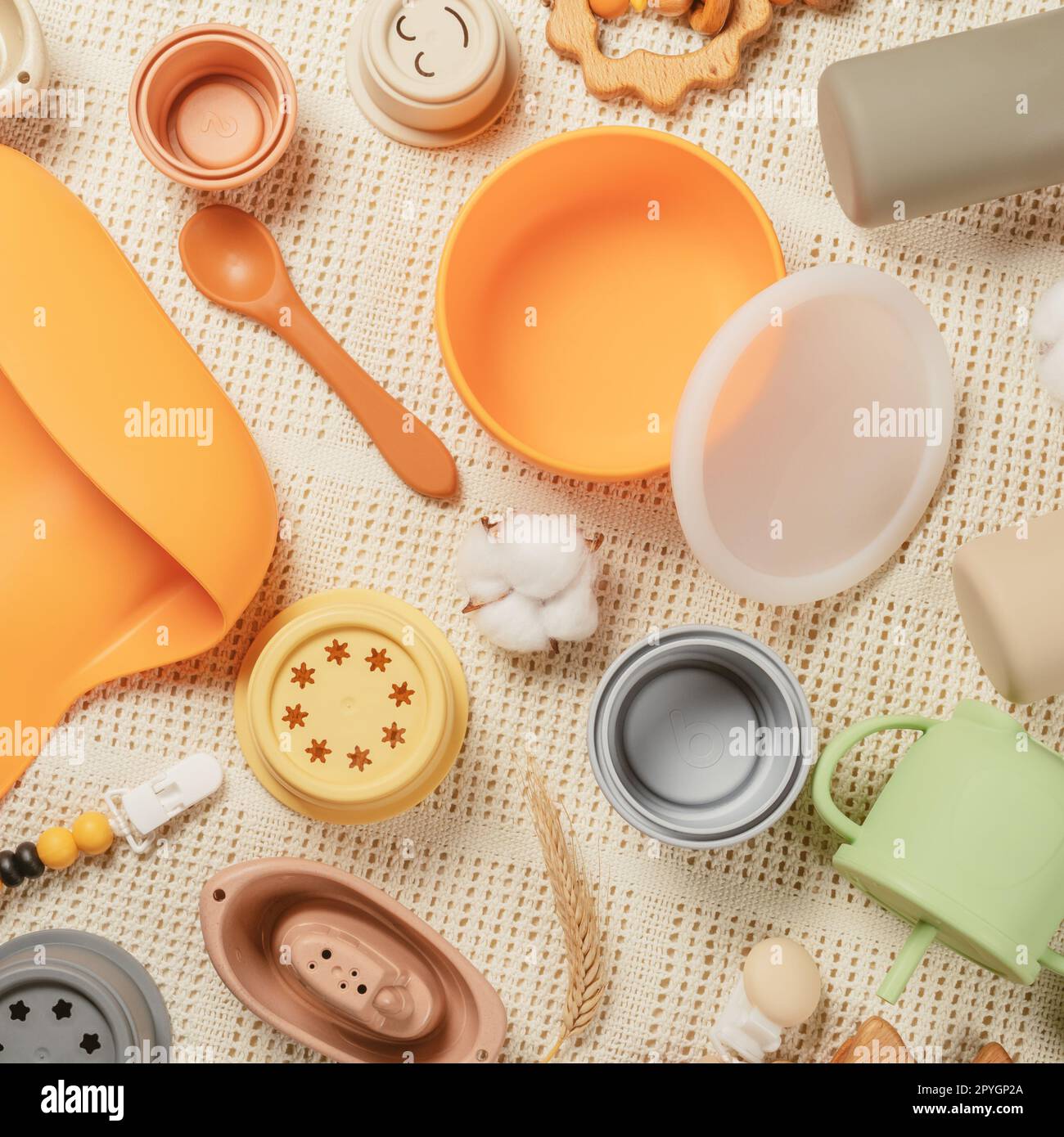 Pastel silicone set of tableware, cutlery, bib, accessories and wooden toys for children on white cloth background. Stock Photo