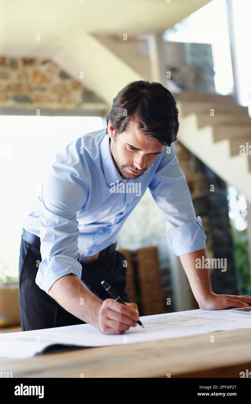 This plan should be ready for approval soon. A young architect doing the final corrections on a floor plan. Stock Photo