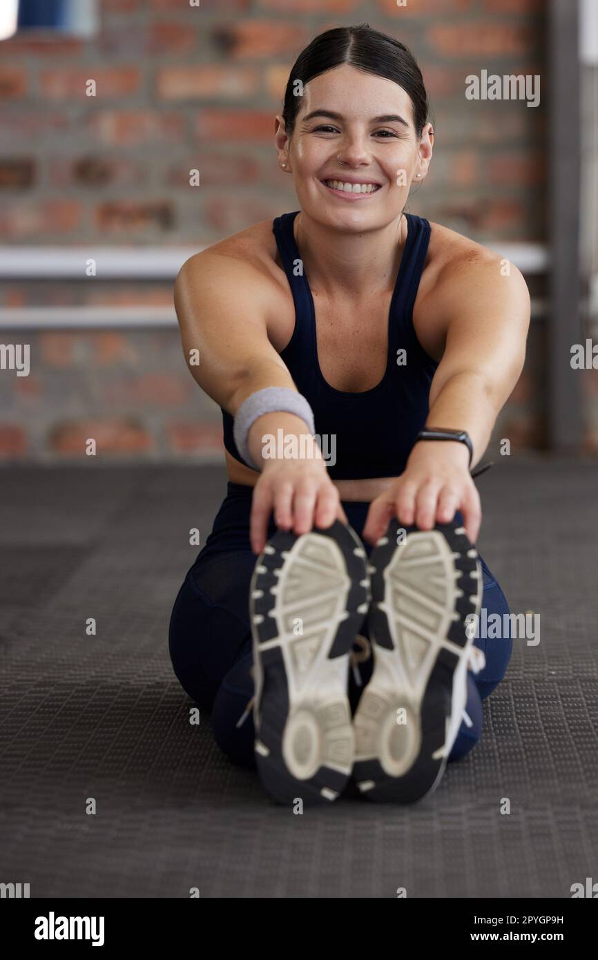 Fitness, woman stretching in gym for workout, body training and start exercise with warm up portrait. Female smile, sports motivation and wellness, strong muscle with pilates and sneakers for workout Stock Photo