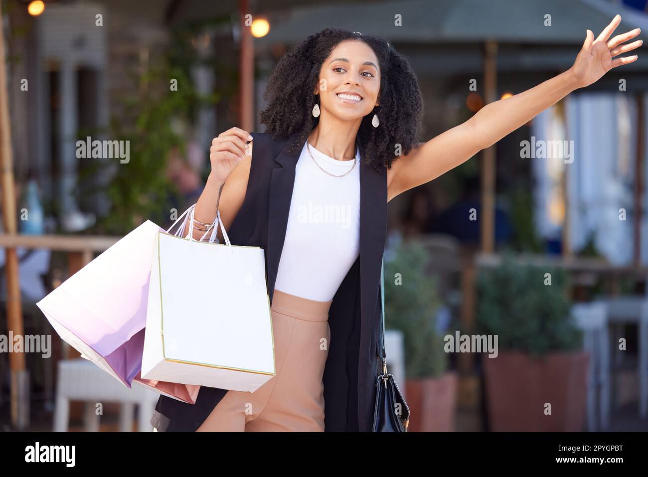 Black woman, shopping and city street as happy customer waves hand for cab or taxi on urban street with retail bags. Travel, fashion and smile of female while waiting for transport outdoor in France Stock Photo