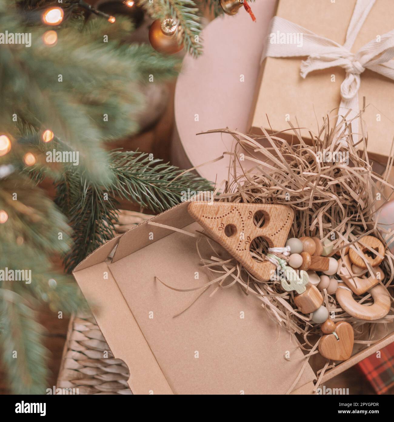 Wooden Christmas tree-shaped children's teether with silicone beads lies among gifts in open box under Christmas tree Stock Photo