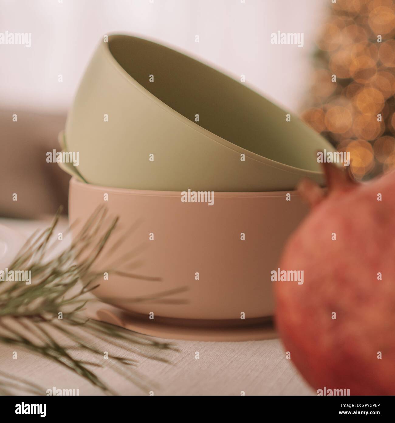 Set of silicone baby dishes. Two bowls stacked against background of Christmas tree. Creative blur. Square frame Stock Photo