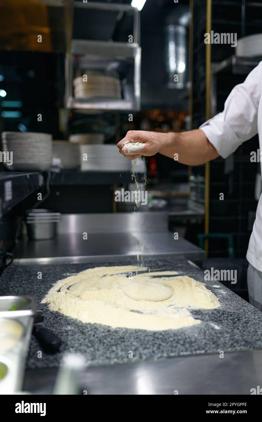 Pastry chef hands sprinkles with flour dough during kneading closeup Stock Photo
