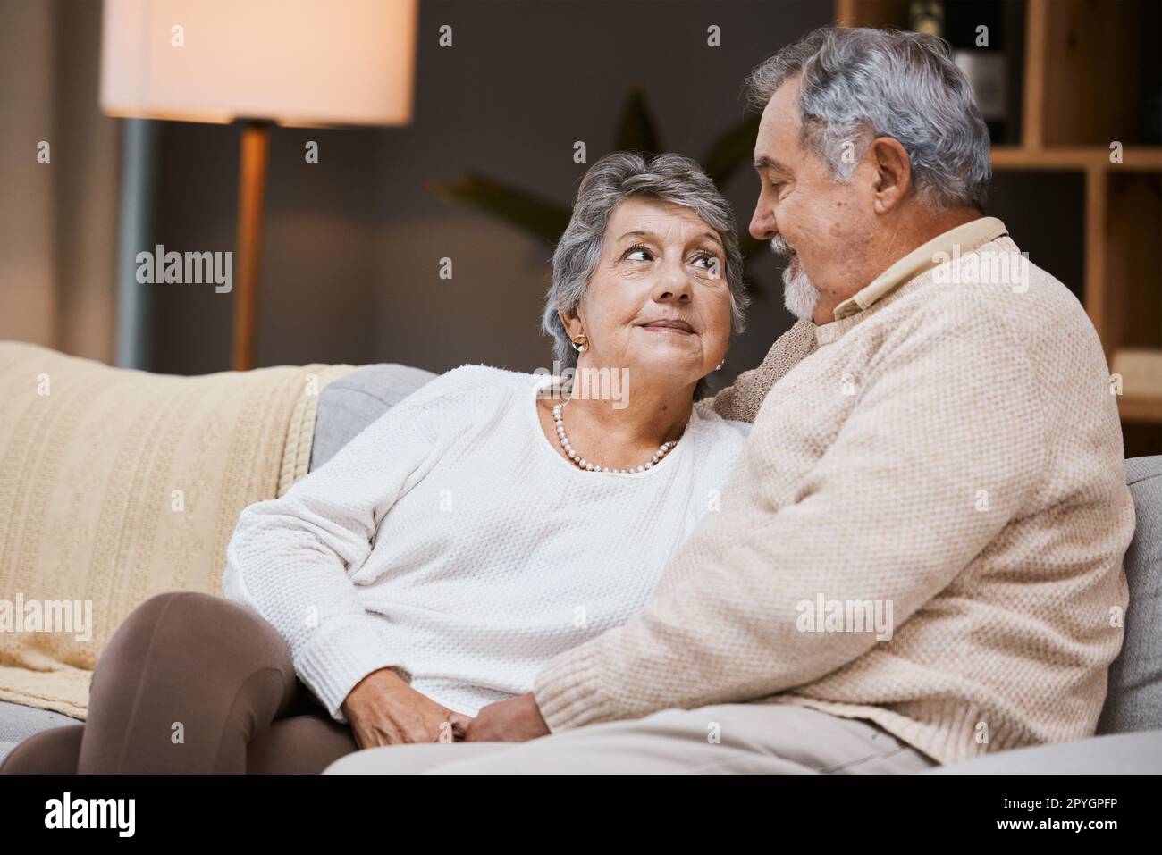 Love, sofa and senior couple talking, marriage and bonding for relationship, retirement and romance. Romantic, elderly man and mature woman in living room, conversation and relax on weekend break. Stock Photo