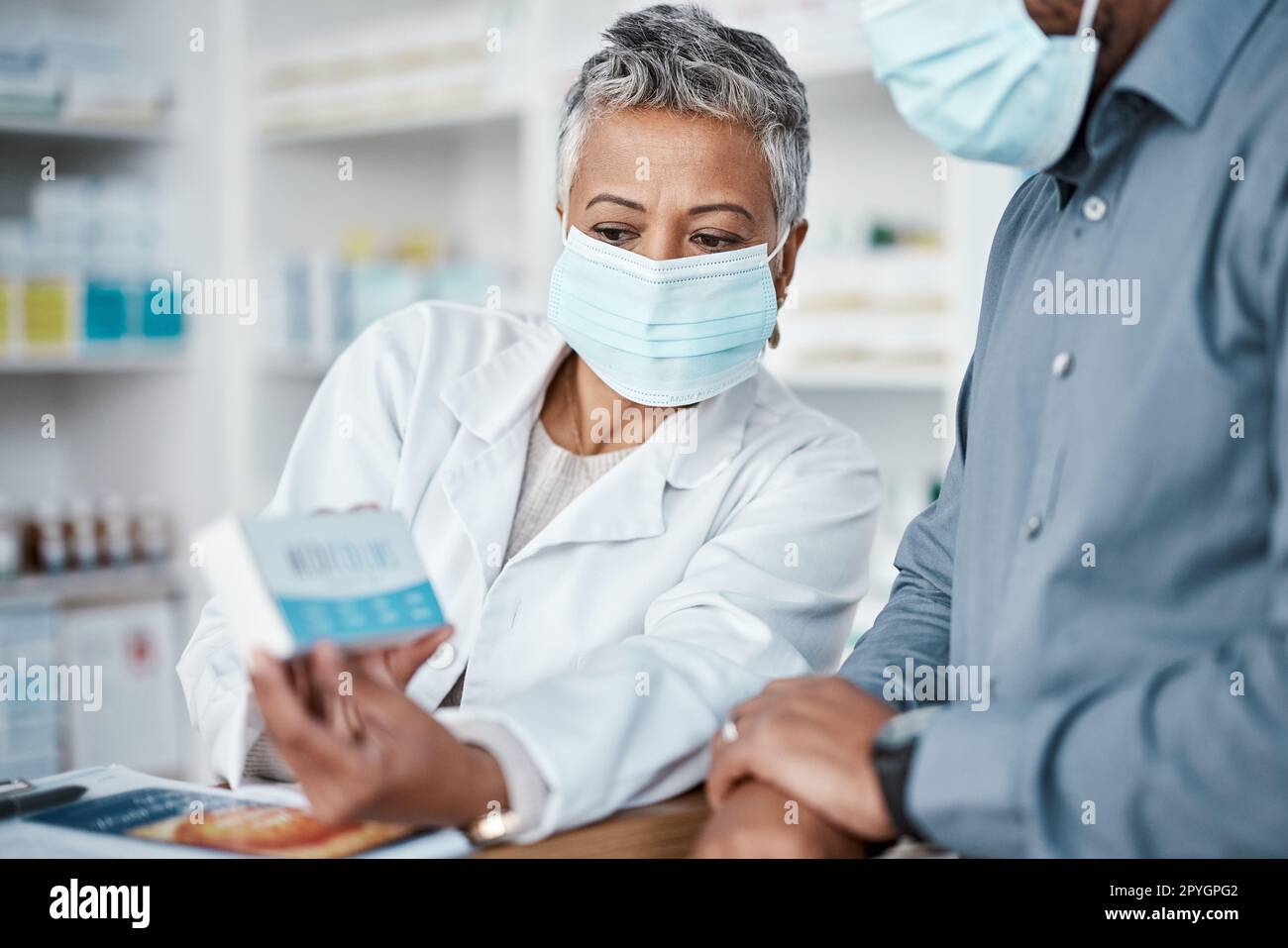 Covid, pharmacy and woman with box consulting patient on prescription, medication or medicine. Corona, healthcare and senior female medical professional showing black man health product in drug store Stock Photo