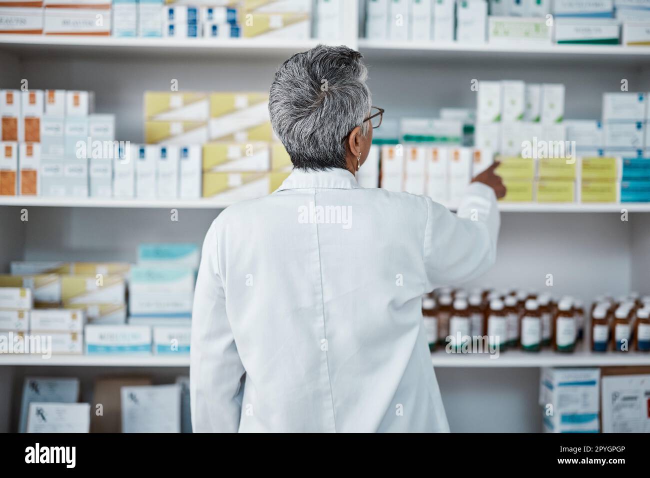 Pharmacy pills, pointing and senior pharmacist with product choice, medicine box or pharmaceutical medication drugs. Retail medical store, healthcare and back of elderly woman point at shop shelf Stock Photo