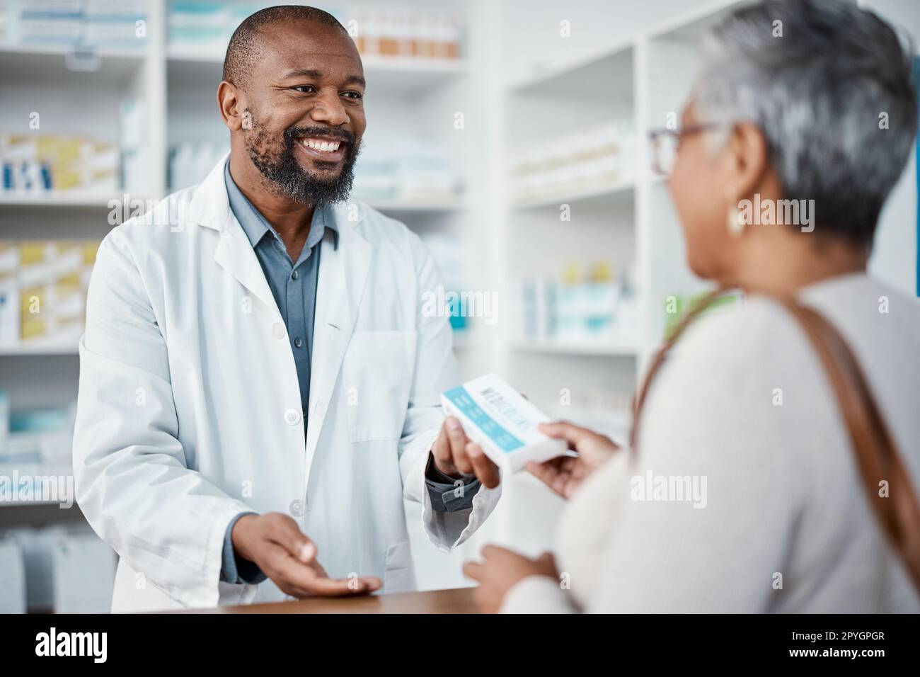 Healthcare, pharmacist and woman at counter with medicine or prescription drugs in hands at drug store. Health, wellness and medical insurance, man and customer at pharmacy for advice and pills. Stock Photo