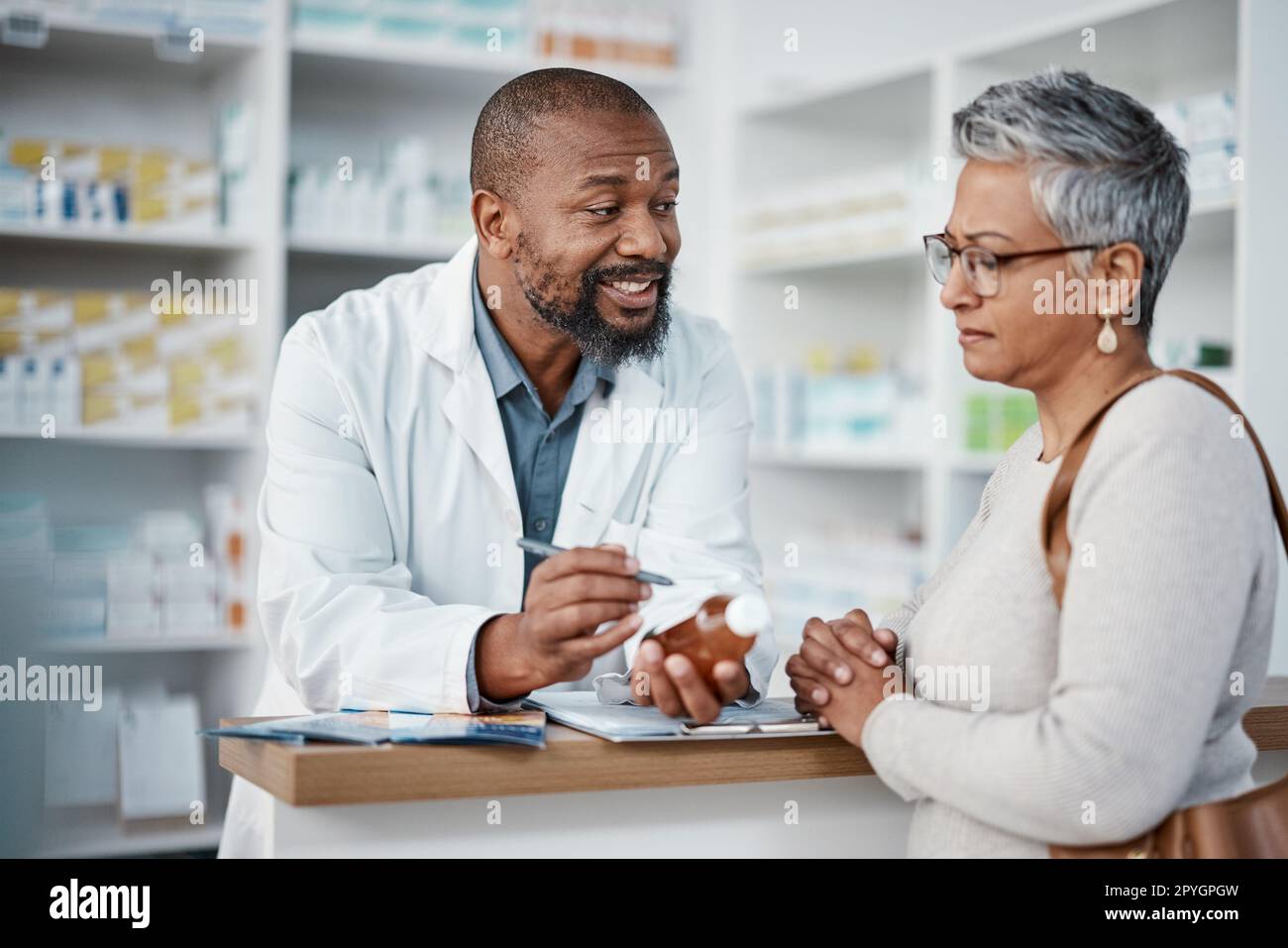 Pharmacy, black man and woman with healthcare medicine and conversation for instructions. Pharmacist, female patient and medical professional talking, stress and explain for customer and frustrated. Stock Photo