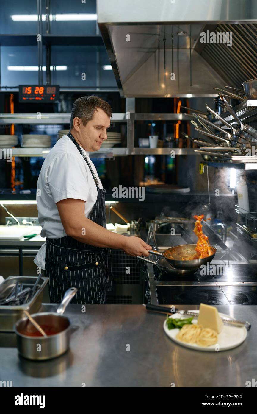 Chef throwing on air hot pasta in frying pan, cooking process Stock