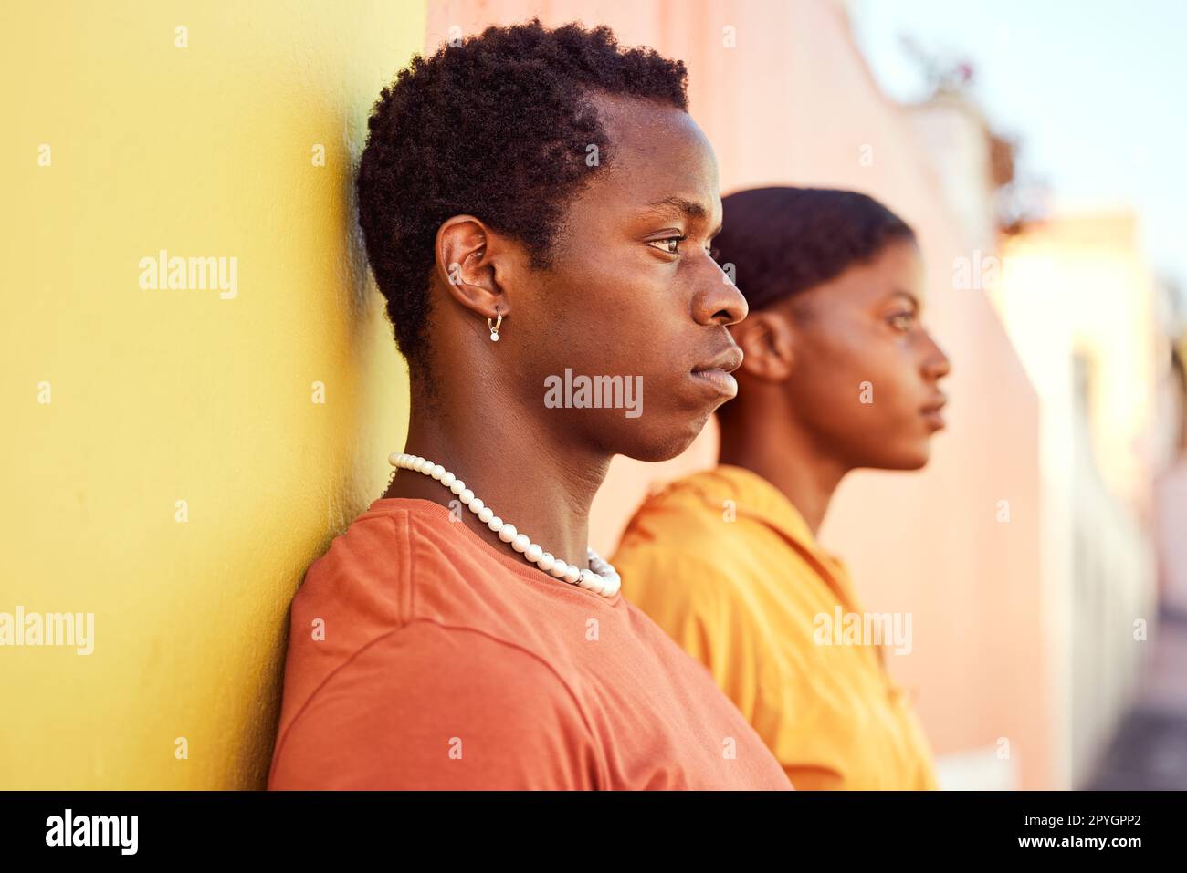 Urban fashion, African people and couple of friends relax with designer brand clothes, casual style and luxury apparel. Gen z aesthetic, color and profile of black woman and man on orange yellow wall Stock Photo