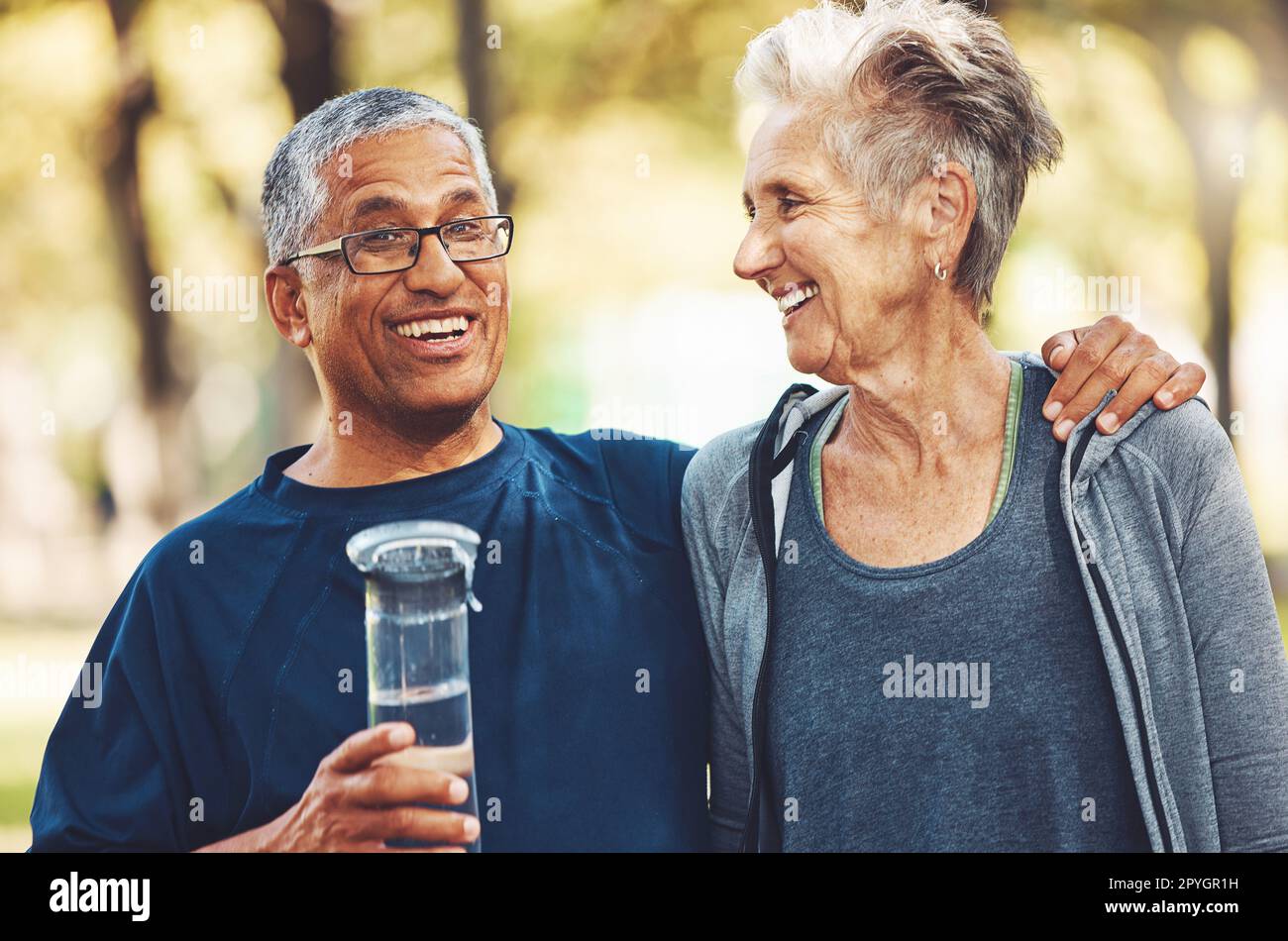 Exercise, senior couple in park and water bottle for training, workout and smile. Mature man, elderly woman and hydration for practice, cardio and energy for wellness, health and fitness in nature. Stock Photo