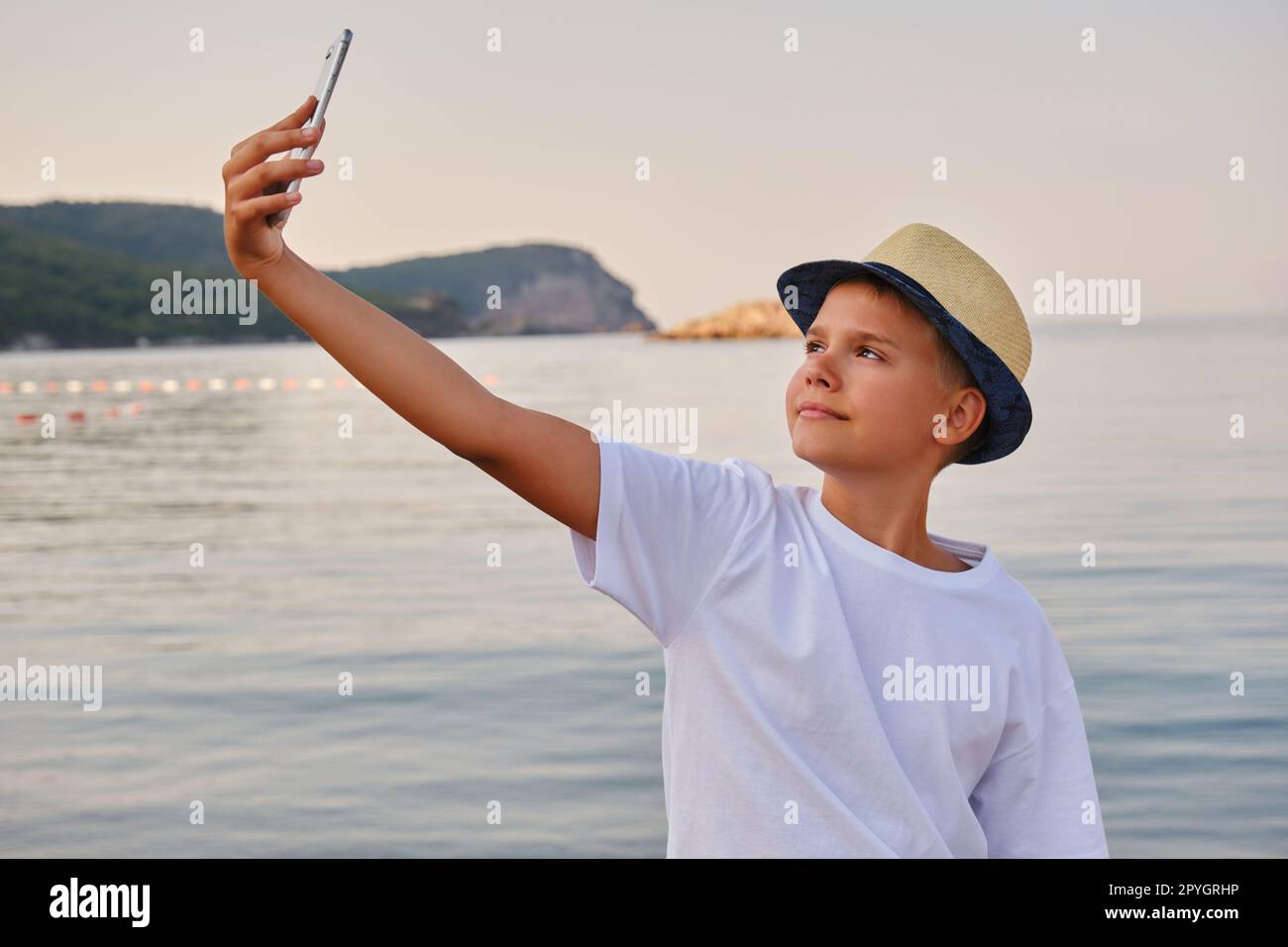 Boy in a hat takes a selfie portrait near the sea. Happy guy enjoying summer holidays at beach Stock Photo