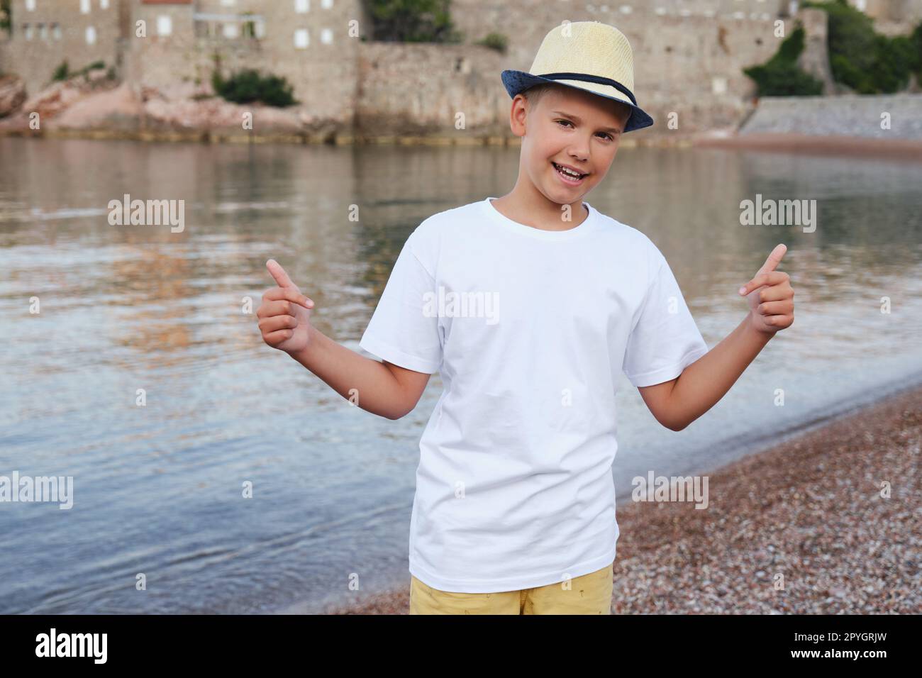 Stylish teen boy on the seashore smiles and points to a white t-shirt. Stock Photo