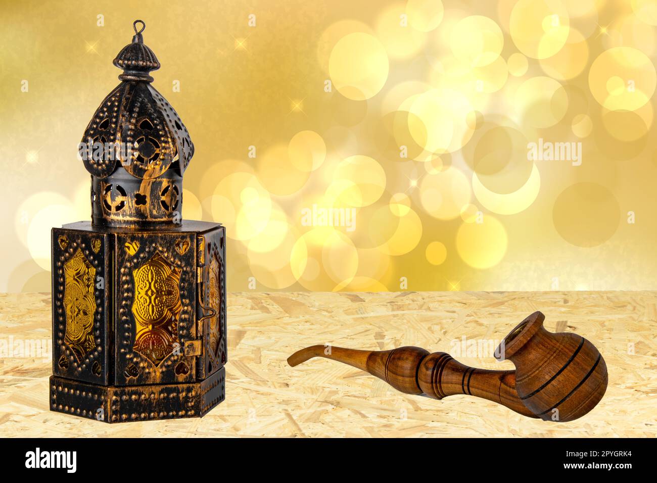 Old oriental or arabic metallic lantern and a handmade wooden tobacco pipe on table over abstract golden stars background. Ramadan Kareem template. Card design. Stock Photo