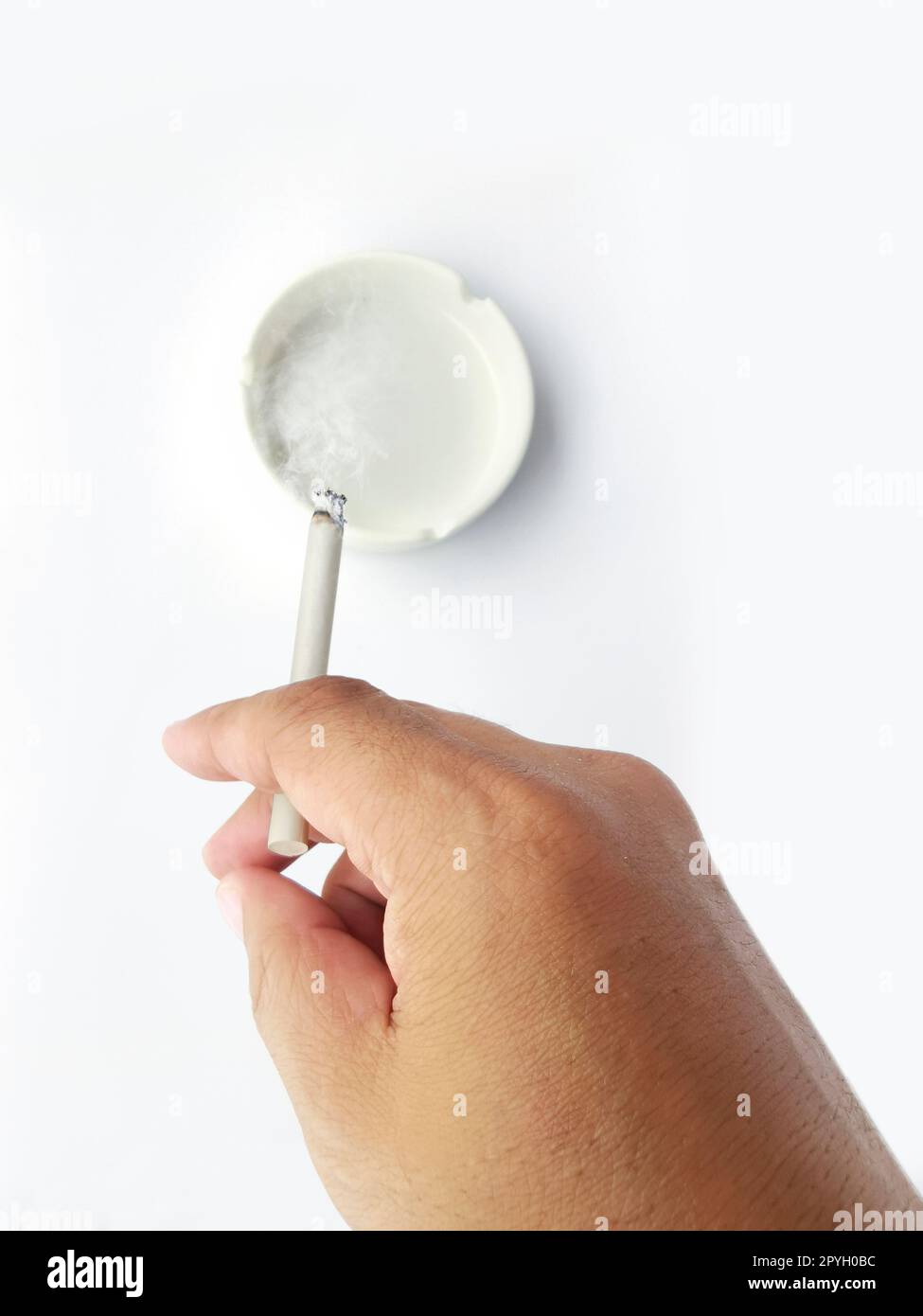 A man's hand flicks the ashes of the burning cigarette in the ashtray. Smoking is harmful to