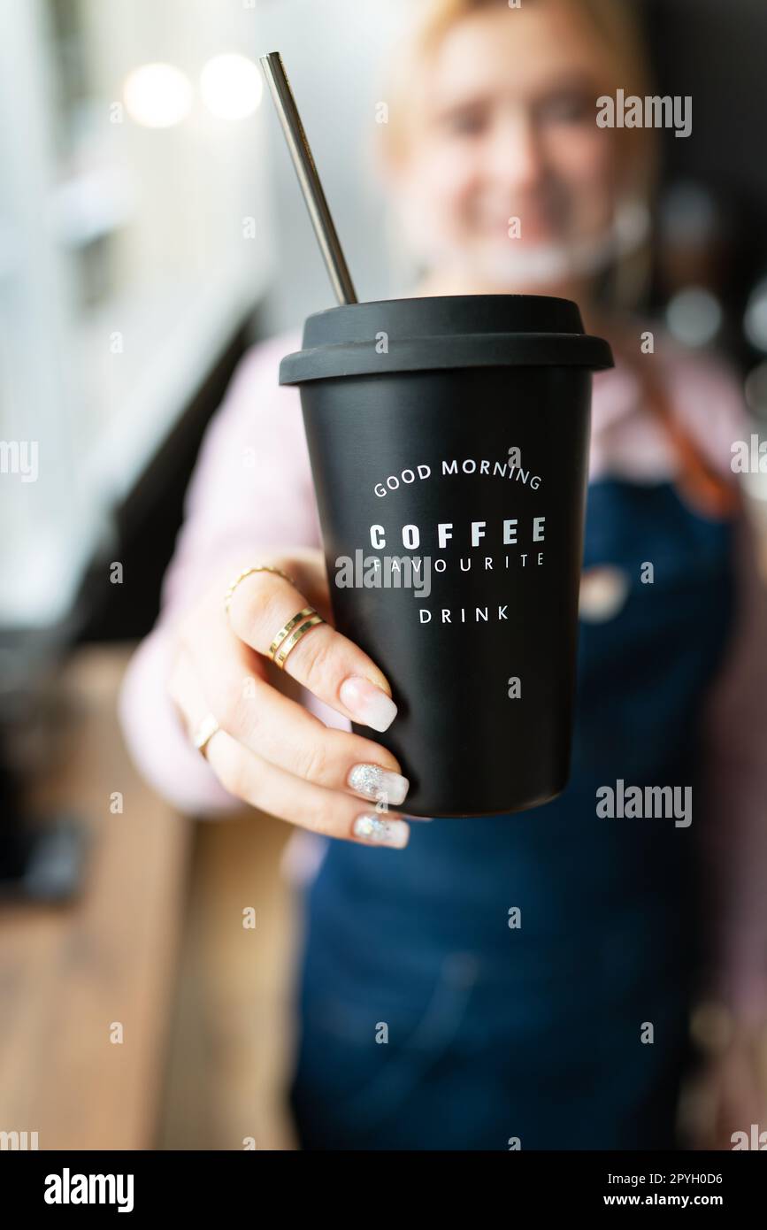 Barista girl holding a black metal glass with the inscription good morning favorite coffee drink in her hands with prepared hot coffee. Professional coffee preparation. Stock Photo