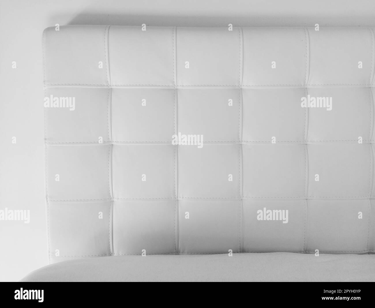 Soft headboard. Upholstery for furniture made of genuine or artificial leather and quilted fabric. Soft headboard against a light wall. Black and white monochrome photo Stock Photo